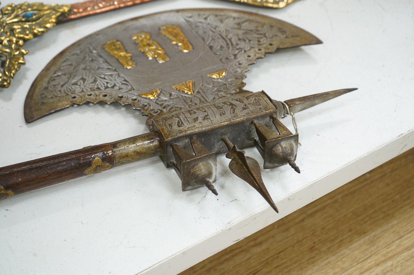 A decorative Indian axe, the large head inlaid with brass Hindu figures, together with a brass mounted North Indian kukri, another similar knife with bone handle, and a large shovel-shaped copper and brass item possibly